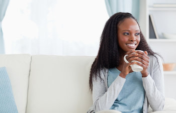 smiling woman with a mug in hand sitting on the couch, 