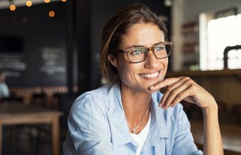 Woman wearing glasses smiles, sitting in a cafe with a relaxed posture., 